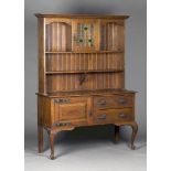 An Edwardian Arts and Crafts oak dresser, the angular pediment above a leaded glass cupboard and