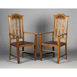 A pair of Edwardian Arts and Crafts oak elbow chairs, probably by Wylie & Lochhead, the arched top