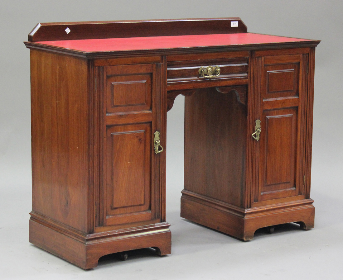 An Edwardian walnut twin pedestal desk, the red leather top above a drawer and two cupboards, raised