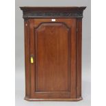 A late George III mahogany hanging corner cabinet, the blind fretwork frieze above an arched panel