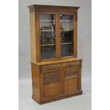 A late Victorian walnut bookcase cabinet, the moulded pediment above a pair of glazed doors, the