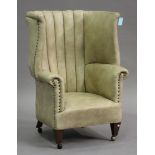 A George V tan leather wing back armchair on square tapering legs and castors, height 110cm, width
