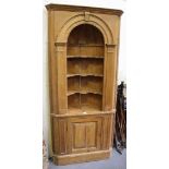 An early 20th century pine corner cabinet with carved foliate decoration, the arched open shelves