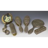 An Indian white metal five piece dressing table set, decorated in relief with figures, buildings and