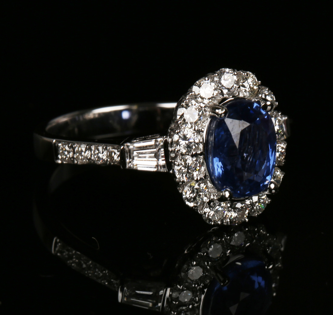 An 18ct white gold, sapphire and diamond cluster ring, claw set with an oval cut sapphire within a