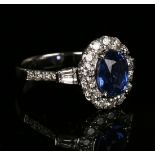 An 18ct white gold, sapphire and diamond cluster ring, claw set with an oval cut sapphire within a
