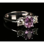 An 18ct white gold, pink sapphire and diamond three stone ring, claw set with the oval cut pink