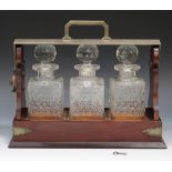 A 20th century plate mounted mahogany three bottle tantalus, fitted with three square cut glass