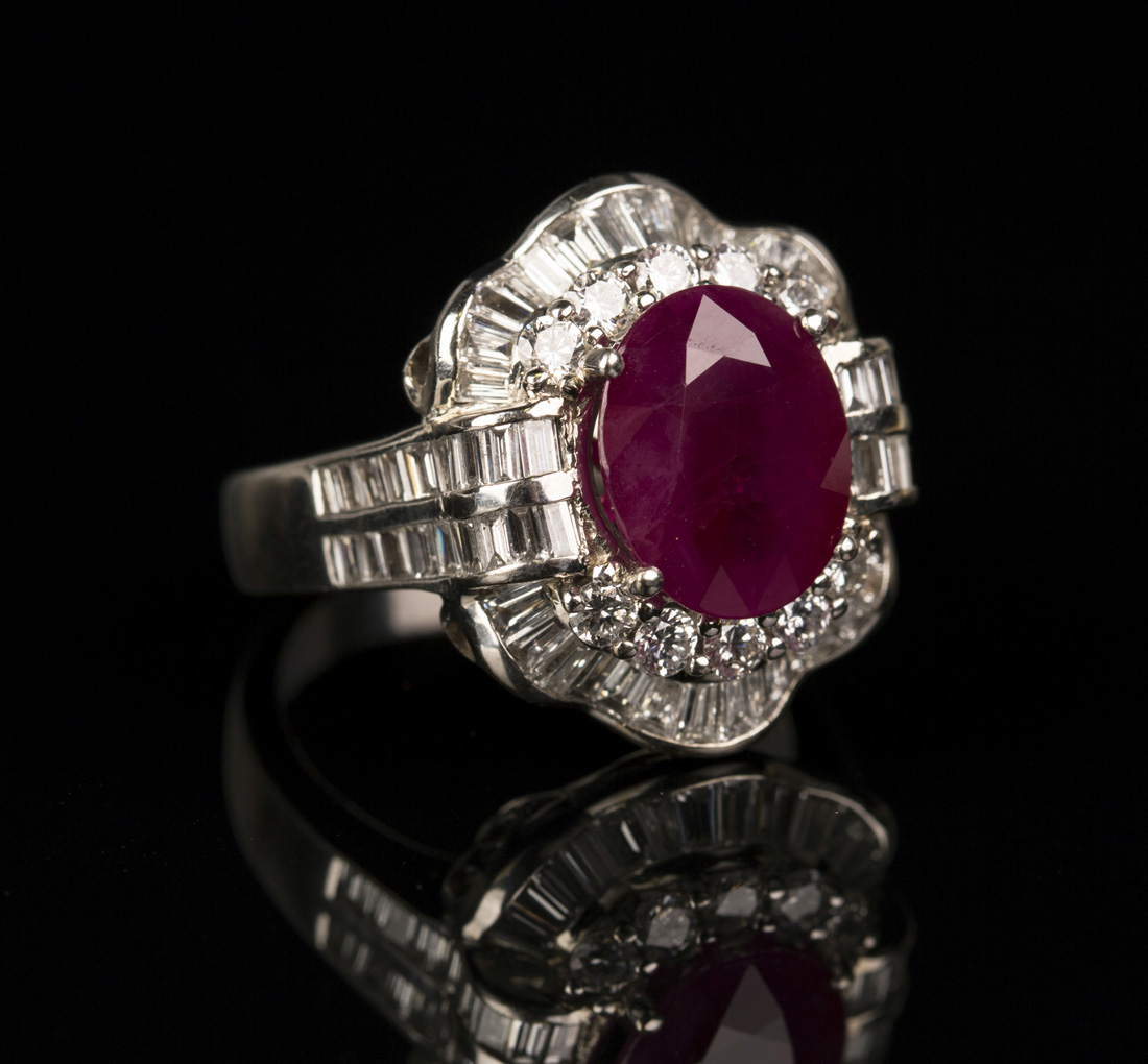 An 18ct white gold, ruby and diamond cluster ring, claw set with an oval cut ruby within a