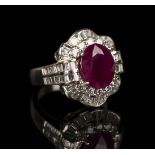 An 18ct white gold, ruby and diamond cluster ring, claw set with an oval cut ruby within a