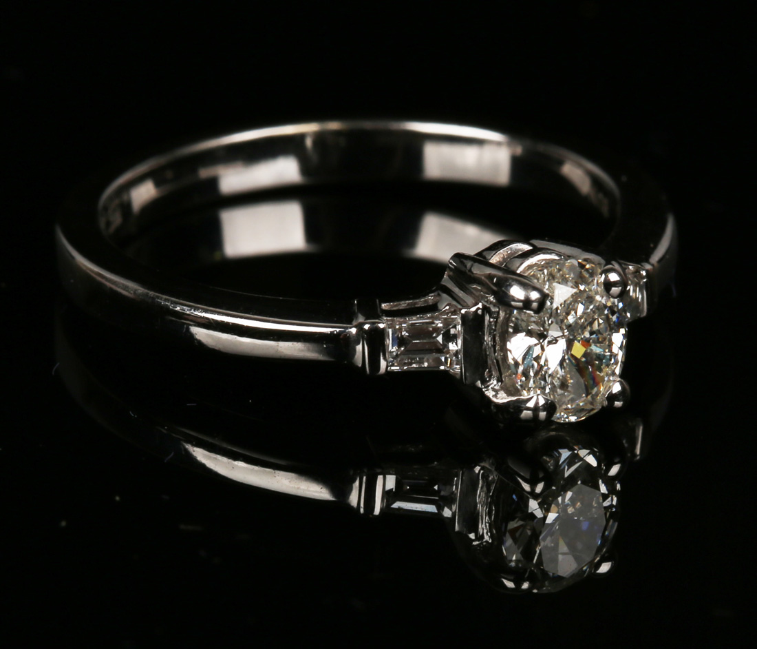 A white gold and diamond ring, claw set with an oval cut diamond between baguette diamond single