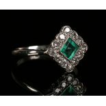 A platinum, emerald and diamond lozenge shaped cluster ring, mounted with the square cut emerald