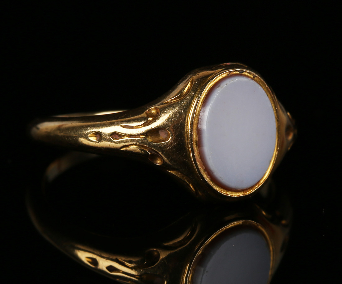 A gold and sardonyx oval signet ring with decorated shoulders, ring size approx N1/2.Buyer’s Premium