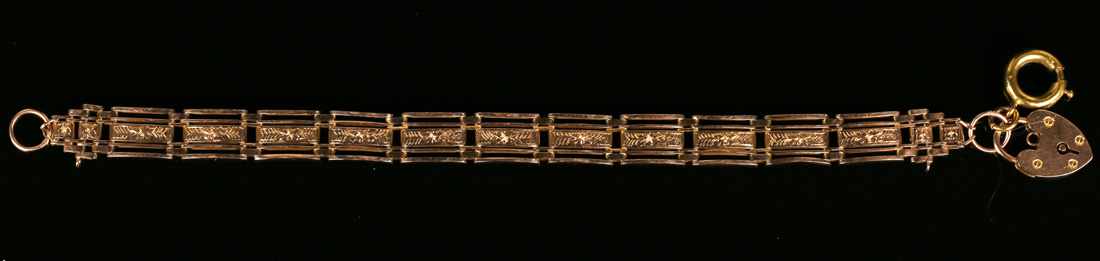 A gold bracelet in a curved bar link design with engraved decoration to the centre, detailed '15ct',