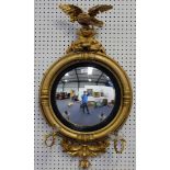 A 19th century gilt convex wall mirror with an eagle surmount and a rounded border with leaf