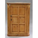 An early 20th century pine corner cabinet, the moulded pediment above a panelled door flanked by