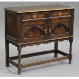 A George V oak side cabinet, the moulded top above two drawers and a pair of carved cupboards, on