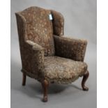 An early 20th century Queen Anne style walnut wing back armchair, the scroll arms and serpentine