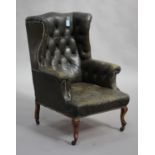 An early 20th century George III style wing back armchair, upholstered in green leather, raised on