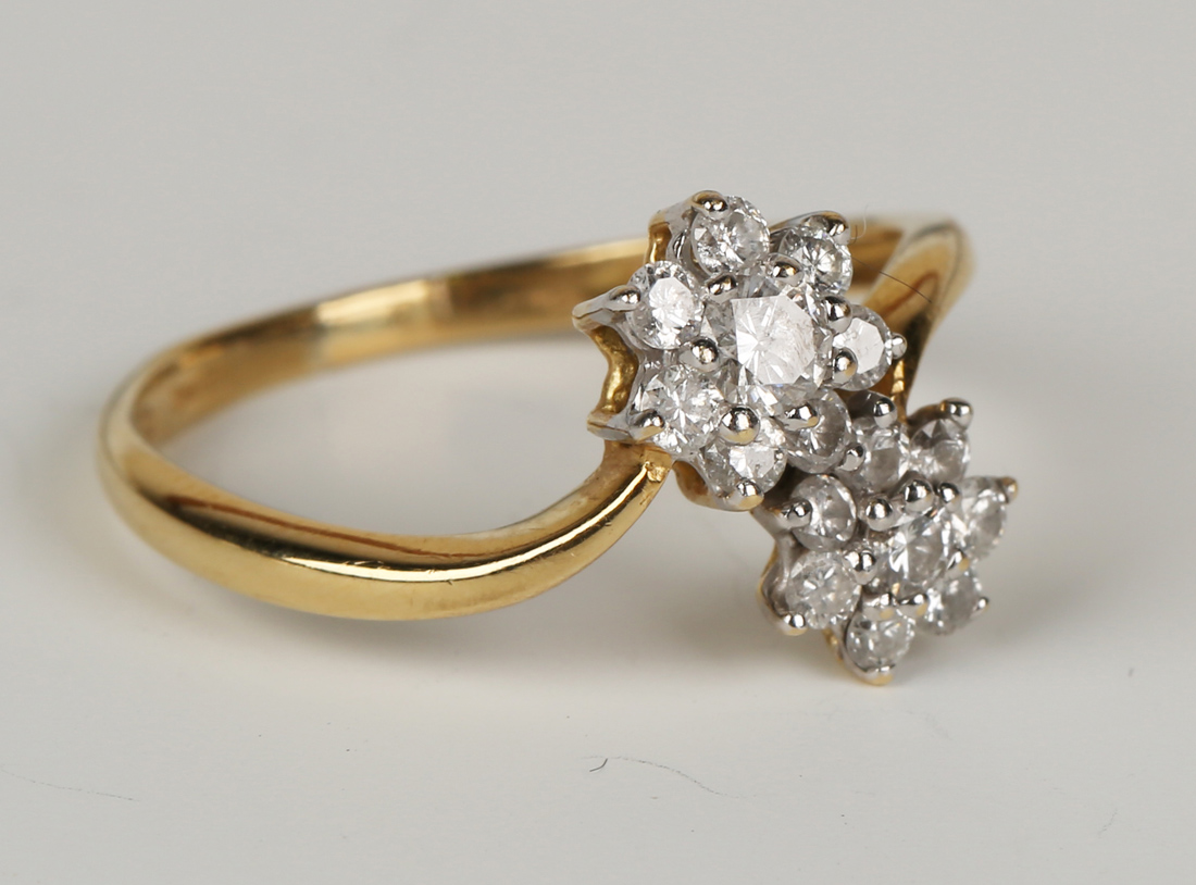 A gold and diamond ring in a twin flowerhead cluster cross-over design, claw set with circular cut