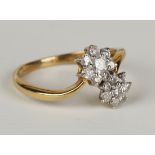 A gold and diamond ring in a twin flowerhead cluster cross-over design, claw set with circular cut