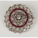 A diamond and ruby brooch in a pierced circular design, claw set with the principal circular cut