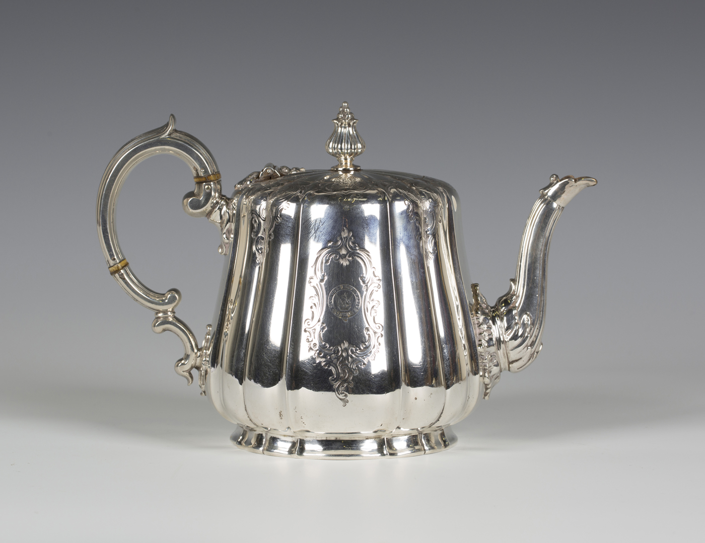 A Victorian silver teapot of shaped circular form, engraved with foliate scroll borders and opposing