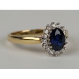 An 18ct gold, sapphire and diamond oval cluster ring, claw set with the oval cut sapphire within a