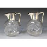 A pair of Victorian silver mounted clear glass claret jugs, each fitted with a cylindrical silver