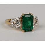 An 18ct gold, emerald and diamond cluster ring, claw set with a rectangular cut emerald between