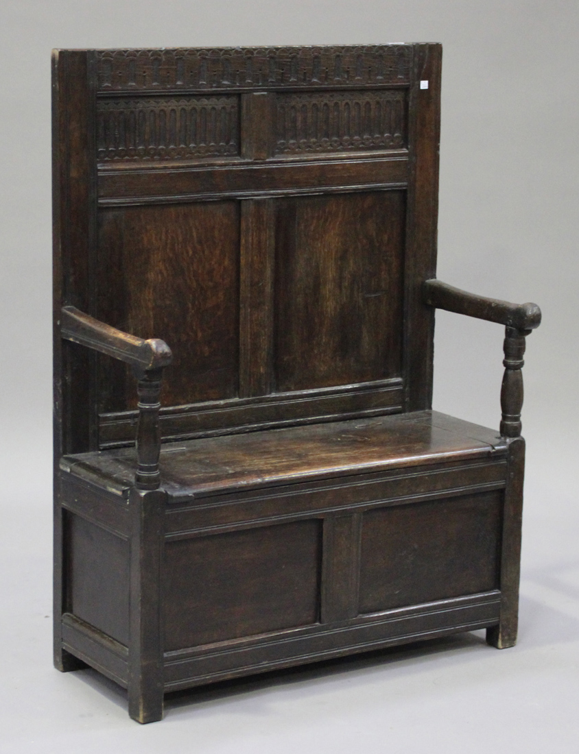 An 18th century and later panelled oak box seat settle with carved decoration, on stile supports,