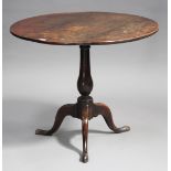 An 18th century oak circular tip-top wine table, raised on a turned column and tripod cabriole legs,