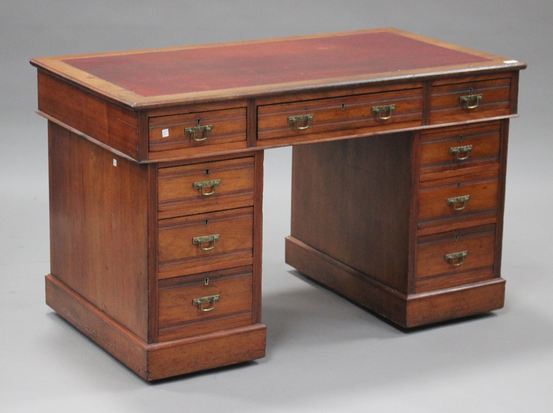 An Edwardian walnut twin pedestal desk, fitted with an arrangement of nine drawers, on plinth bases,