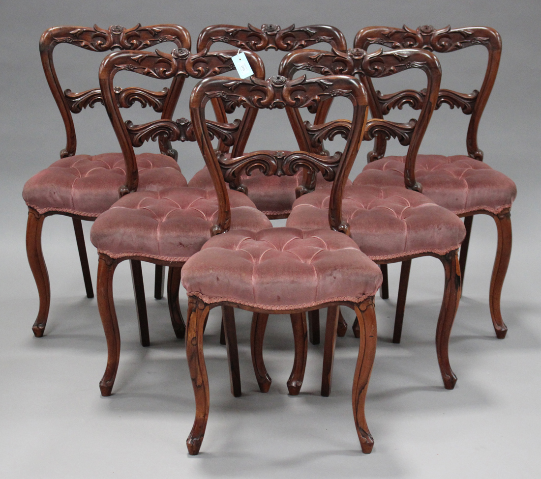 A set of six early Victorian rosewood dining chairs with carved foliate backs, the overstuffed seats