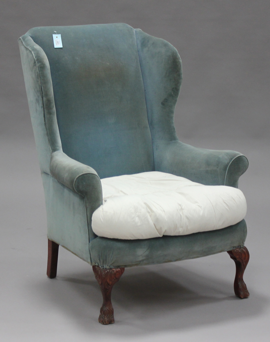 An early 20th century George III style wing back armchair, upholstered in green velour, on carved