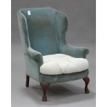 An early 20th century George III style wing back armchair, upholstered in green velour, on carved