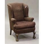 A 20th century George III style wing back armchair, upholstered in purple fabric, raised on carved