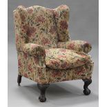 An early 20th century George III style wing back armchair, upholstered in floral damask, raised on
