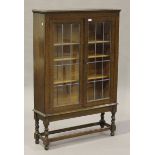 A George V oak glazed bookcase, fitted with two leaded glass doors, on barley twist and block