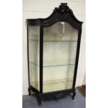 An early 20th century ebonized vitrine, the shaped pediment with a carved floral surmount above a