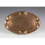 An Arts and Crafts copper oval tray of hammered form, the raised undulating border worked with a