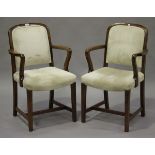 A pair of early 20th century oak framed elbow chairs, upholstered in cream fabric, raised on block