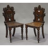 A pair of late Victorian mahogany hall chairs with carved cartouche backs and solid seats, on turned