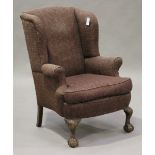 An early 20th century Queen Anne style wing back armchair with scroll arms and bowfront seat, raised