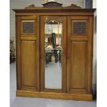 A late Victorian walnut wardrobe, the carved pediment above a central mirrored door flanked by