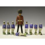 Eight all-bisque soldiers standing to attention, each wearing a blue jacket and white trousers, on