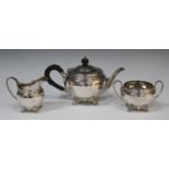 A George VI silver three-piece tea set of circular faceted form, raised on scroll feet, comprising