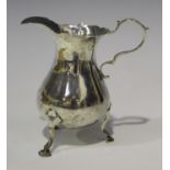 A mid-18th century silver cream jug of low bellied form with scroll handle and wavy rim, raised on