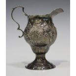 A George III silver cream jug of ogee baluster form with scroll handle, decorated in relief with