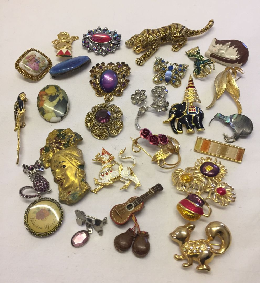 A tub with a good quantity of costume jewellery brooches to include a cat set with purple stones